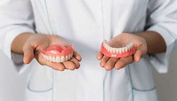 Person in white coat holding upper and lower dentures