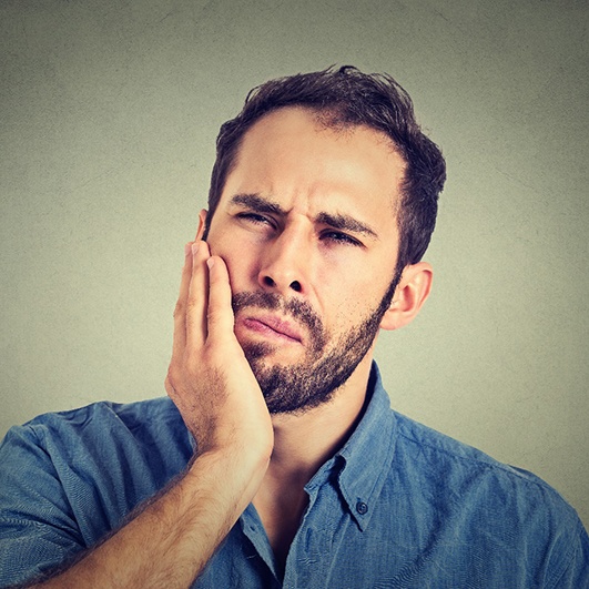 Bearded man rubbing jaw and looking concerned