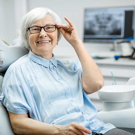 Senior woman with glasses sitting in dental chair and smiling